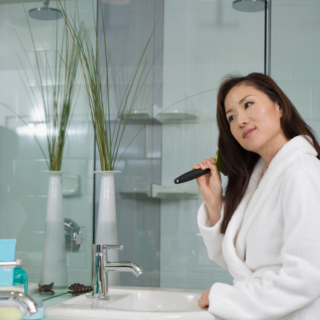 A woman is brushing her teeth in front of a mirror, showcasing her Loxxie Hair while maintaining her oral care.