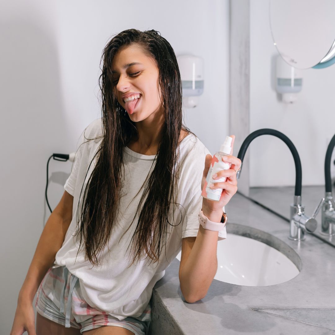 A woman is brushing her teeth in front of a mirror, showcasing her Loxxie Hair while maintaining her oral care.