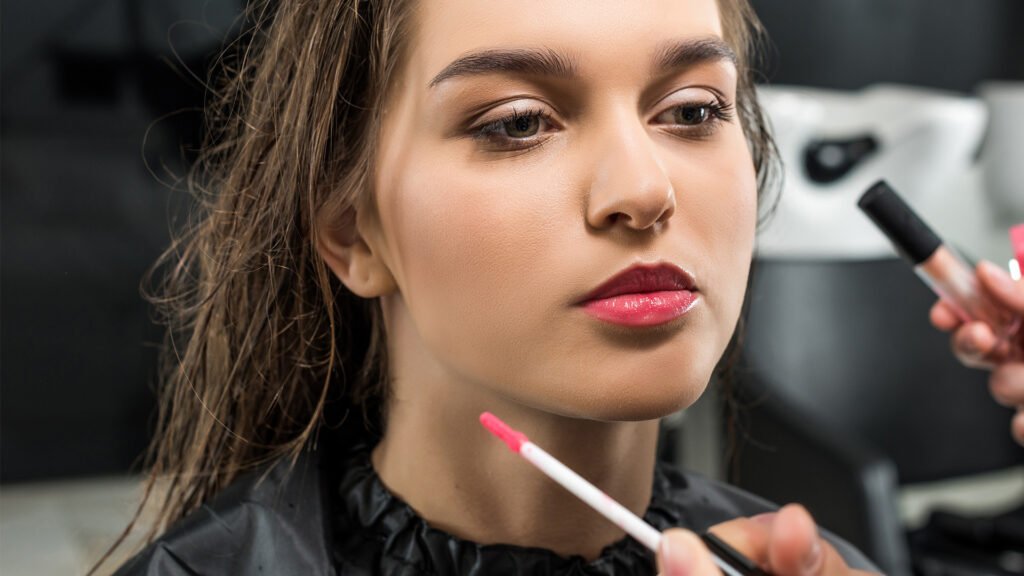 A woman receives makeup application from a professional artist at Loxxie Hair studio.