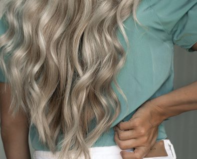 A woman with long blonde hair holds a Loxxie Hair spray bottle, showcasing her hair care routine.